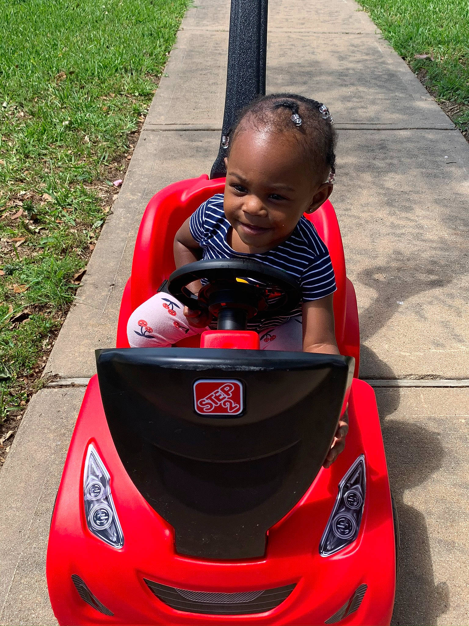 Jayci is registered to the contest to win money with this photo: automotive_design, automotive_exterior, bumper, car, child, compact_car, cool, driving, facial_expression, fun, grass, joy, luxury_vehicle, person, plant, product, red, smile, summer, toddler