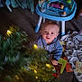 Brentlee is registered to the contest to win money with this photo: toddler, child, blue_hoodie, indoor, carpet, toy, blanket, christmas_tree, lights, holiday, curious, face, person, floor, play_area, baby, furniture, cozy, warm_light, festive