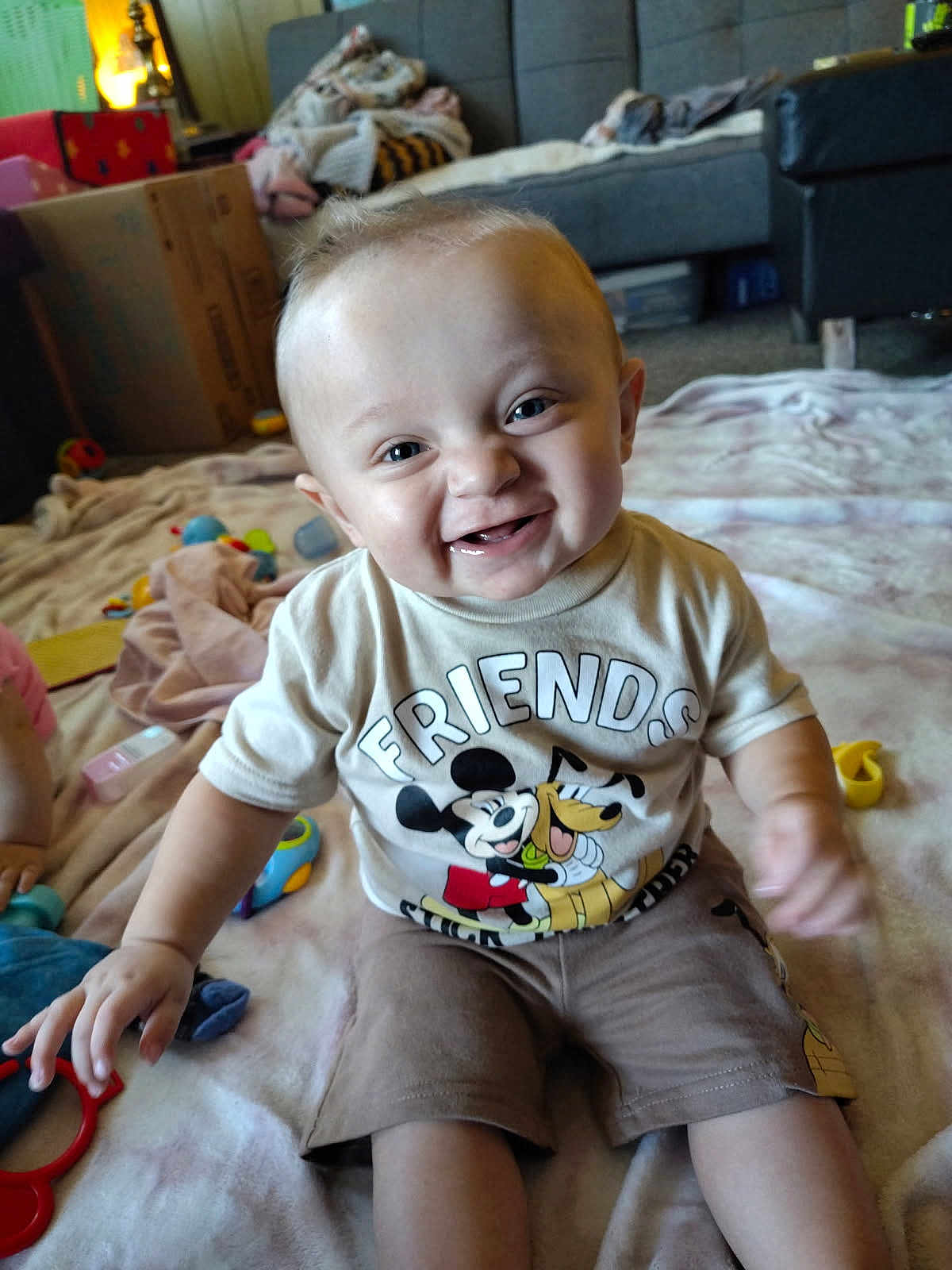 Brentlee joined the competition — help win amazing prizes! baby, child, smiling, tshirt, mickey_mouse, pluto, friends, indoor, blanket, toys, happy, sitting, living_room, furniture, cute, infant, playtime, clothing, person, portrait