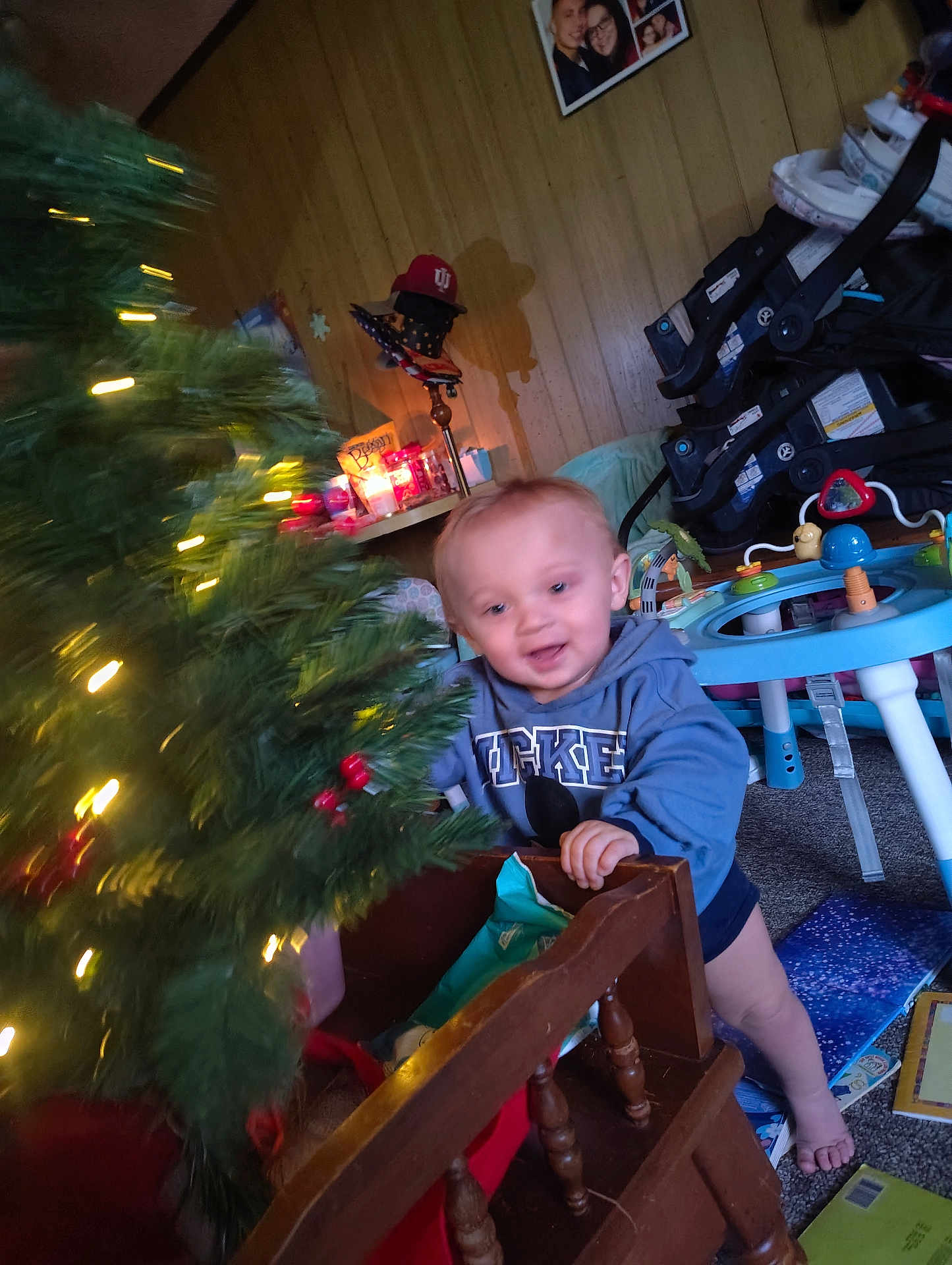 Brentlee joined the competition — help win amazing prizes! toddler, child, christmas_tree, holiday_lights, toy, indoor, baby_gear, hoodie, mickey_mouse, carpet, wood_paneling, furniture, play_area, smiling, barefoot, decorations, candle, cozy, family_photo, home