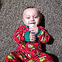 Brentlee joined the competition — help win amazing prizes! baby, child, bottle, pajamas, red_clothing, grinch_pattern, carpet, floor, smile, happy, infant, lying_down, indoors, cute, holding, person, young_child, cozy, festive, hand