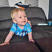 Cole is registered to the contest to win money with this photo: toddler, child, crawling, blue_shirt, couch, living_room, smiling, happy, blonde_hair, indoor, cushion, fabric, furniture, person, casual_clothing, baby, young_child, home, playful, relaxed