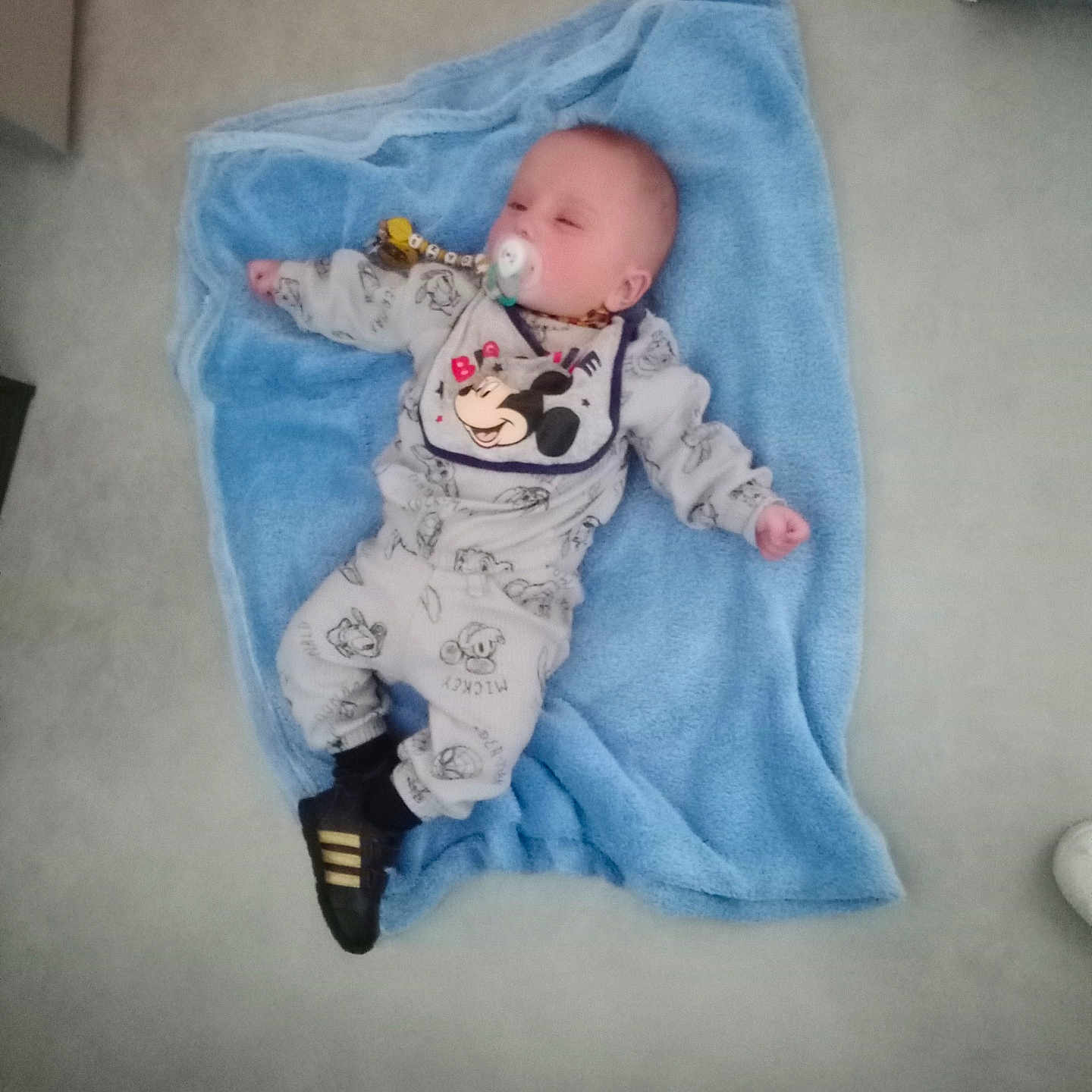 Ezyo participe au concours pour gagner de l'argent avec cette photo : baby, blanket, blue, child, clothing, comfort, cute, floor, footwear, indoor, infant, lying_down, mickey_mouse, pacifier, pajamas, person, resting, sleeping, small, toy