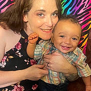 Eric is registered to the contest to win money with this photo: woman, child, smiling, holding, colorful_background, rainbow, zebra_stripes, happy, portrait, indoor, casual_clothing, baby, toddler, person, face, pattern, fabric, joy, family, candid
