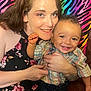 woman, child, smiling, holding, colorful_background, rainbow, zebra_stripes, happy, portrait, indoor, casual_clothing, baby, toddler, person, face, pattern, fabric, joy, family, candid