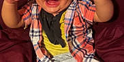 Eric joined the competition — help win amazing prizes! baby, child, smiling, laughing, plaid_shirt, yellow_shirt, shorts, barefoot, sitting, couch, maroon, indoor, happy, joyful, arms_raised, infant, cute, portrait, person, clothing