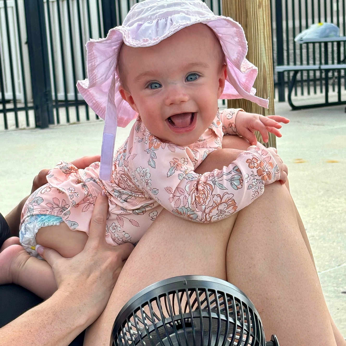 Oakley Grace is registered to the contest to win money with this photo: baby, child, cute, daylight, fan, fence, hand, happy, hat, infant, legs, outdoor, person, picnic_table, pink_clothing, playful, skin, smiling, summer, sunhat