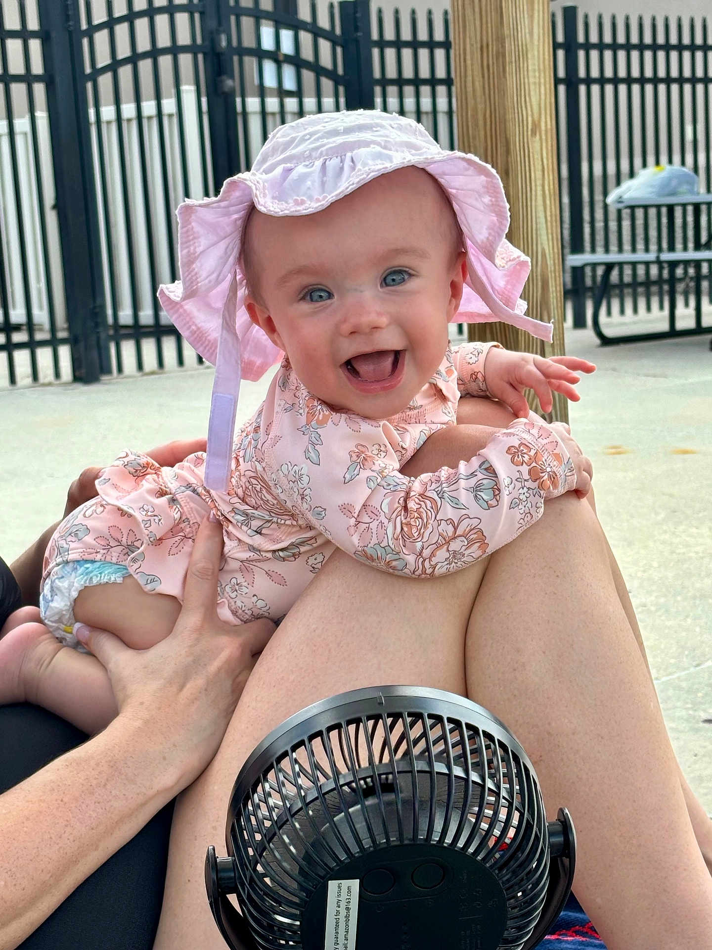 Oakley Grace is registered to the contest to win money with this photo: baby, infant, smiling, hat, pink_clothing, outdoor, legs, hand, fan, picnic_table, fence, sunhat, happy, person, skin, summer, daylight, playful, child, cute