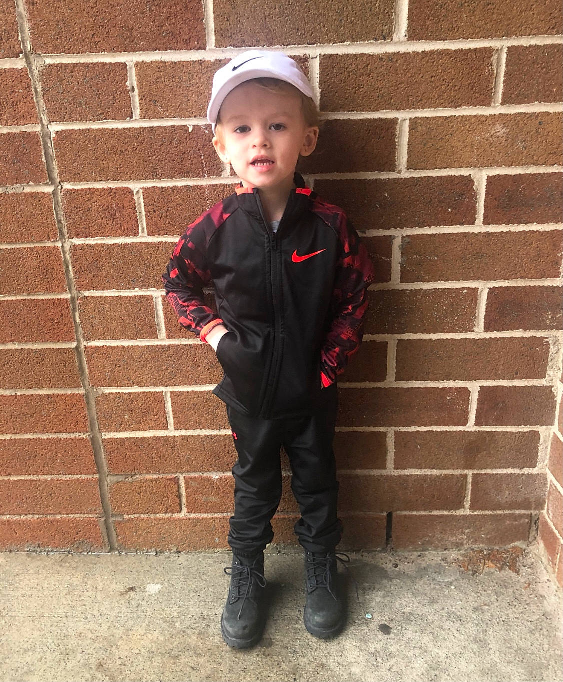 Kayden joined the competition — help win amazing prizes! baby_toddler_clothing, brick, brickwork, cap, carmine, child, clothing, concrete, flooring, footwear, formal_wear, hat, headwear, outerwear, pattern, person, personal_protective_equipment, sleeve, smile, standing