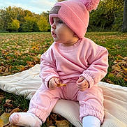 Aria is registered to the contest to win money with this photo: baby, child, pink_clothing, pink_hat, pom_pom_hat, socks, leaf, blanket, grass, autumn_leaves, outdoor, park, trees, fall, nature, side_profile, cute, infant, sitting, daylight