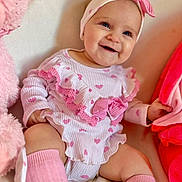 Aria is registered to the contest to win money with this photo: baby, infant, smiling, pink, headband, heart_pattern, sitting, plush_toy, soft_toys, cute, child, clothing, sock, happy, portrait, indoors, comfort, cute_expression, baby_girl, warm_colors