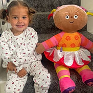River is registered to the contest to win money with this photo: child, girl, pigtails, smiling, stairs, carpet, stuffed_doll, toy, white_clothing, red_sneakers, indoor, happy, seated, playful, person, cute, colorful, plush, patterned_clothing, home