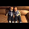 babies, infants, twins, children, couch, sitting, indoors, portrait, pacifiers, matching_outfits, overalls, smiling, faces, siblings, furniture, living_room, cushions, black_background, photograph, cute