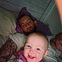 baby, bed, candid, casual, child, closeup, clothing, face, family, happy, head, indoor, man, person, pillow, portrait, relaxing, resting, smiling, tattoos