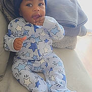 Axel is registered to the contest to win money with this photo: baby, blanket, blue_hat, child, couch, cozy, curious, expression, face, hand_near_mouth, hat, indoor, infant, onesie, portrait, relaxing, seated, soft_furniture, star_pattern, warm_clothing