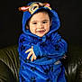 blue_clothing, boy, casual_clothing, child, cozy, crossed_arms, cute, dark_background, face, happy, headwear, hoodie, indoor, leather_chair, paw_prints, person, portrait, sitting, smiling, young_child