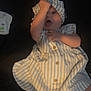 baby, child, infant, striped_dress, hat, arm, hand, face, lying_down, dark_background, diaper_pack, skin, cute, chubby_cheeks, clothing, button, playful, indoors, person, portrait
