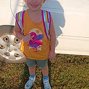 Emma is registered to the contest to win money with this photo: backpack, car, casual_clothing, child, cute, daytime, flamingo_print, girl, grass, happy, orange_shirt, outdoor, pink_bow, shadow, shorts, smiling, sneakers, standing, sunlight, tire