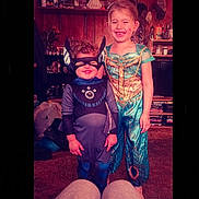 Stephen is registered to the contest to win money with this photo: child, costume, superhero, mask, smile, indoor, carpet, shelf, toy, figurine, dress, happy, person, play, childhood, room, furniture, curly_hair, blonde_hair, casual