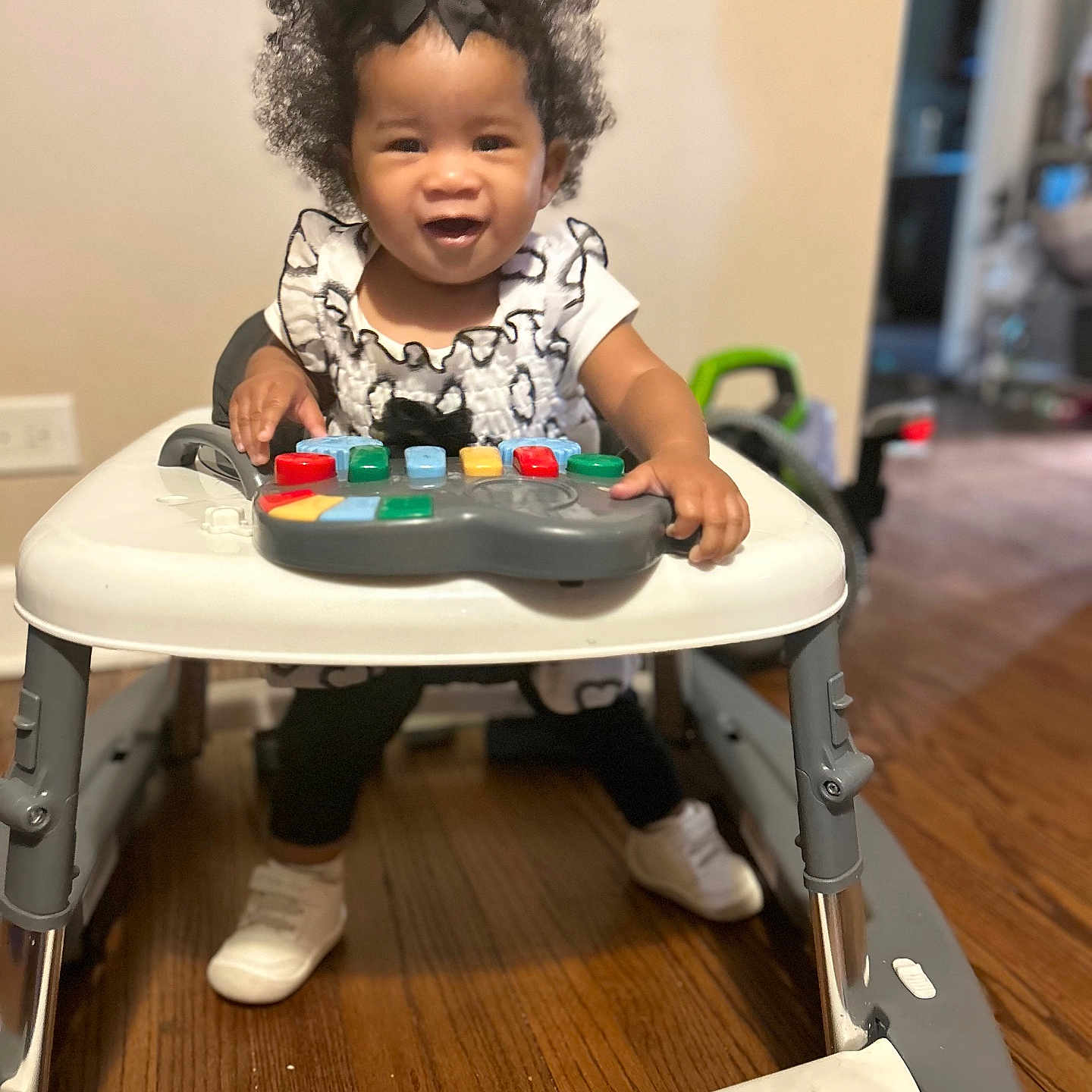 Five is registered to the contest to win money with this photo: activity, baby, bow, child, clothing, colorful, curly_hair, floor, furniture, happy, home, indoor, person, play, shoes, smile, toddler, toy, walker, wood_floor