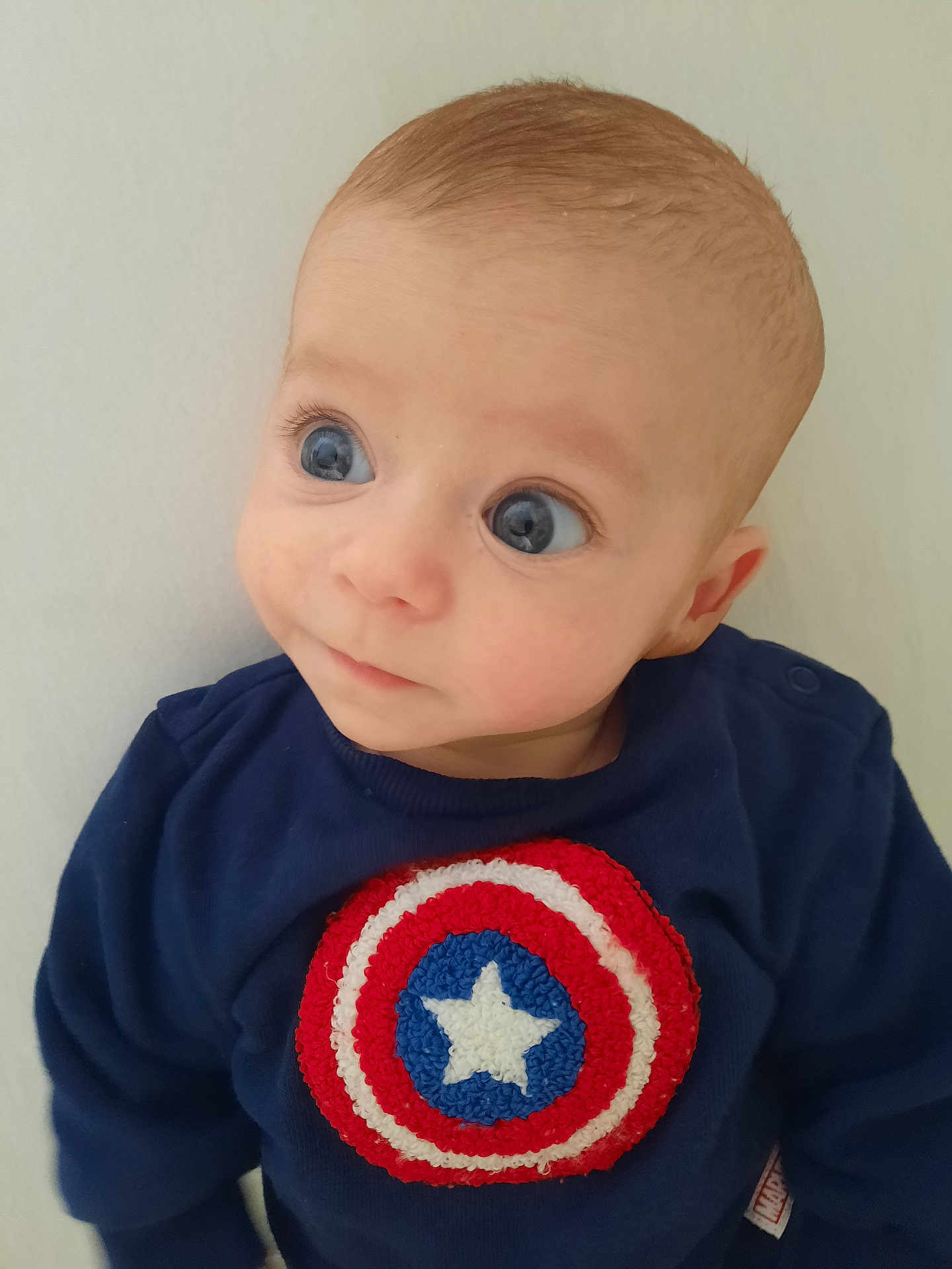 Leonardo a rejoint le concours — aidez-le/la à gagner de superbes lots ! baby, child, infant, face, blue_eyes, sweater, captain_america, superhero_logo, curious_expression, portrait, close_up, cute, young_child, clothing, casual_wear, indoor, light_background, head, person, looking_away