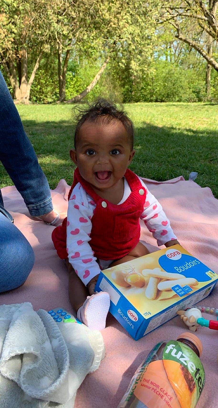 Yaëlle a rejoint le concours — aidez-le/la à gagner de superbes lots ! baby, baby_toddler_clothing, child, event, food, fun, grass, happy, lap, leisure, person, picnic, plant, play, recreation, sharing, sitting, smile, toddler, tree