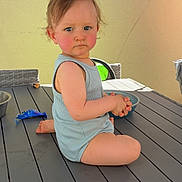 Mensïo participe au concours pour gagner de l'argent avec cette photo : toddler, child, sitting, table, outdoor, romper, blue_clothing, wicker_chair, bowl, sunlight, rosy_cheeks, hair, hands, face, expression, gray_table, wall, porch, serious, person