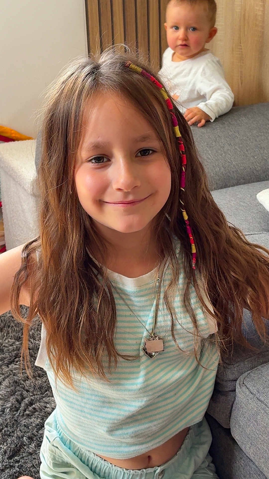 Layana participe au concours pour gagner de l'argent avec cette photo : child, girl, toddler, smile, hair_wrap, necklace, striped_shirt, indoor, couch, carpet, curious, happy, portrait, casual_clothing, home, furniture, person, long_hair, sitting, playful