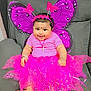 baby, child, smiling, costume, butterfly_wings, pink_tutu, headband, bracelet, sofa, indoor, cute, happy, portrait, infant, decorative, bright_colors, playful, accessories, feet, seated