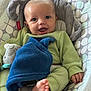 baby, smiling, infant, green_clothing, blue_blanket, plush_toy, baby_seat, cushion, patterned_fabric, happy, small_hand, small_foot, indoor, portrait, cute, child, cozy, soft_texture, closeup, person