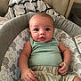 baby, infant, child, cushion, seat, clothing, green_top, shorts, indoor, home, furniture, blanket, pattern, face, skin, hand, expression, cute, comfort, relax