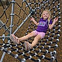 child, girl, playground, rope_net, smiling, purple_shirt, pink_shorts, sneakers, outdoor, play, happy, metal_structure, wood_chips, summer, casual_clothing, recreation, fun, young, leisure, daytime