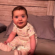 Harley is registered to the contest to win money with this photo: baby, child, infant, bed, pillow, wooden_headboard, polka_dot, clothing, socks, frills, indoors, portrait, cute, smiling, sitting, person, face, skin, eyes, young