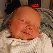 Hunter is registered to the contest to win money with this photo: baby, sleeping, infant, smile, white_clothing, blanket, cozy, face, peaceful, indoors, resting, newborn, soft, warm, portrait, cute, child, head, comfort, relaxation