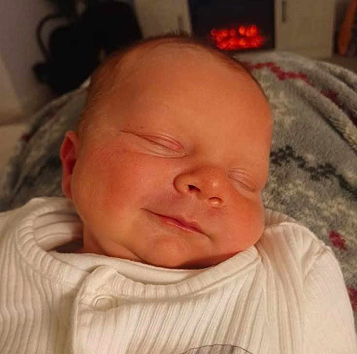 Hunter is registered to the contest to win money with this photo: baby, sleeping, infant, smile, white_clothing, blanket, cozy, face, peaceful, indoors, resting, newborn, soft, warm, portrait, cute, child, head, comfort, relaxation