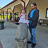 Abigail is registered to the contest to win money with this photo: adult, bench, blue_sky, building, casual_clothing, child, concrete_floor, concrete_statue, cow_statue, daylight, dress, happy, holding_hands, man, outdoor, pigtails, portrait, rocking_chair, smiling, toddler
