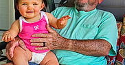 Abigail joined the competition — help win amazing prizes! baby, barefoot, blue_shorts, casual_clothing, chair, child, elderly_man, family, glasses, hand_holding, happy, hat, outdoor, patterned_fabric, people, pink_shirt, porch, seated, smiling, toddler