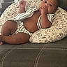 baby, child, infant, couch, pillow, striped_clothing, snack, indoor, staircase, curious, brown_skin, sitting, relaxed, home, soft_lighting, portrait, furniture, hand, face, comfort