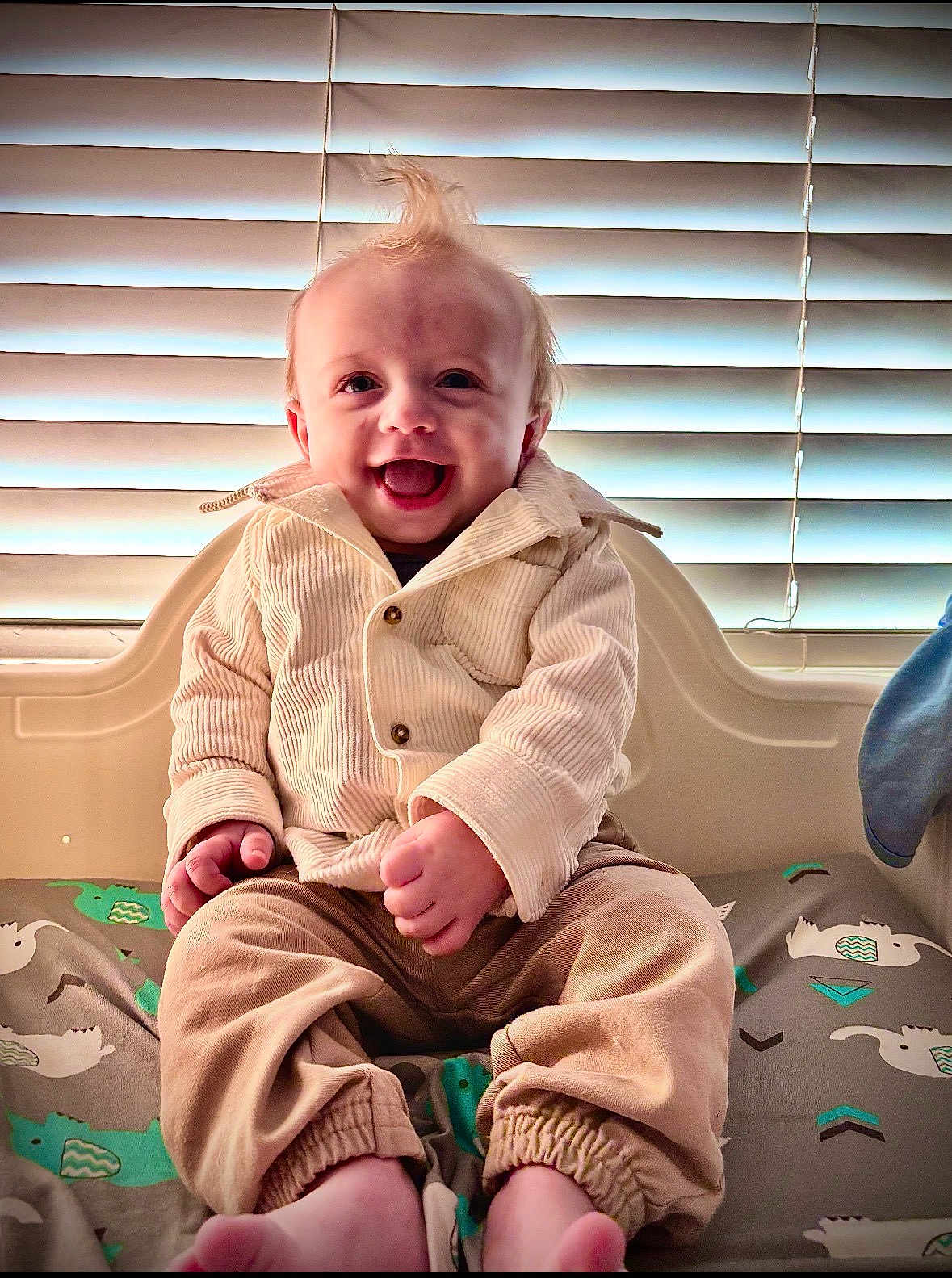 Xavier is registered to the contest to win money with this photo: baby, blinds, child, corduroy, cushion, cute, face, hair, happy, indoor, infant, jacket, light, pants, pattern, person, sitting, smiling, toes, window
