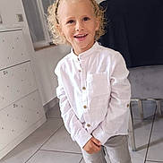 Tiago a rejoint le concours — aidez-le/la à gagner de superbes lots ! blond_hair, cabinet, casual_clothing, chair, child, curly_hair, grey_pants, happy, headband, indoor, light, person, portrait, smiling, standing, tile_floor, white_shirt, white_sneakers, window, young