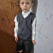 Lochlin joined the competition — help win amazing prizes! black_shoes, boy, casual_pose, child, curly_hair, earring, expression, fashion, floor, formal_clothing, gray_vest, indoor, light_shadow, portrait, shorts, standing, textured_wall, white_shirt, wooden_door, young_boy