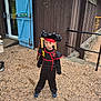 black_clothing, blue, building, child, costume, door, gravel, hat, imaginative, ninja, outdoor, person, pirate, playful, red, rustic, serious_expression, shoes, standing, young