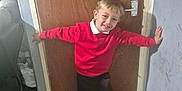 Lochlin is registered to the contest to win money with this photo: arms_outstretched, black_shoes, black_shorts, boy, casual_clothing, child, couch, door, door_handle, flooring, happy, home, indoors, light, playful, red_sweater, smile, wall, wooden_door, young_child
