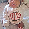 Xymir is registered to the contest to win money with this photo: baby, child, infant, portrait, smiling, sitting, knit_hat, pumpkin, pumpkin_shirt, festive, socks, clothing, bed, bedding, indoor, home, wide_eyes, looking_at_camera, cute, seasonal