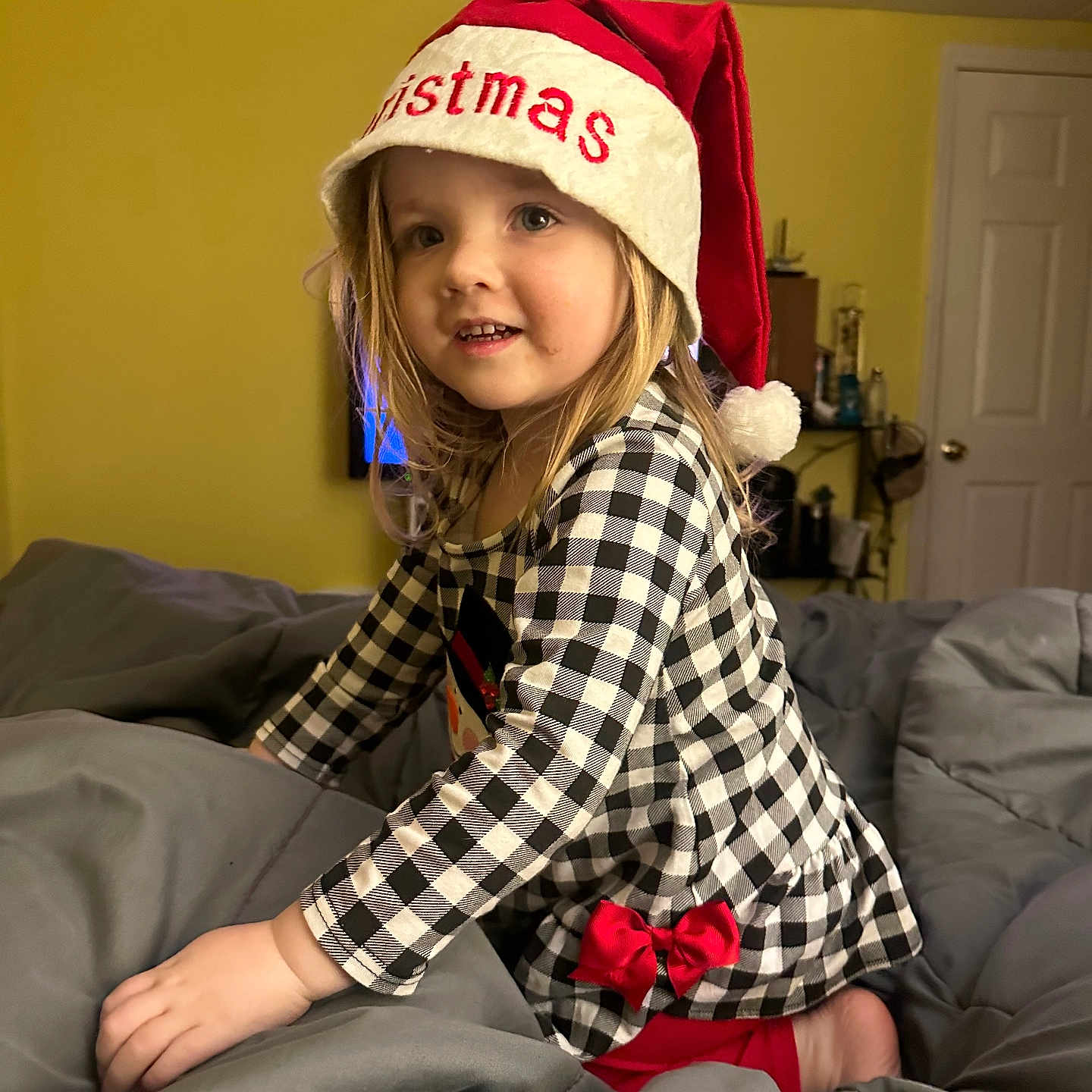 Aurora joined the competition — help win amazing prizes! bedroom, blanket, blonde_hair, checkered_dress, child, christmas_hat, cute, door, festive, furniture, happy, holiday, home, indoor, person, portrait, red_bow, smiling, toddler, yellow_wall