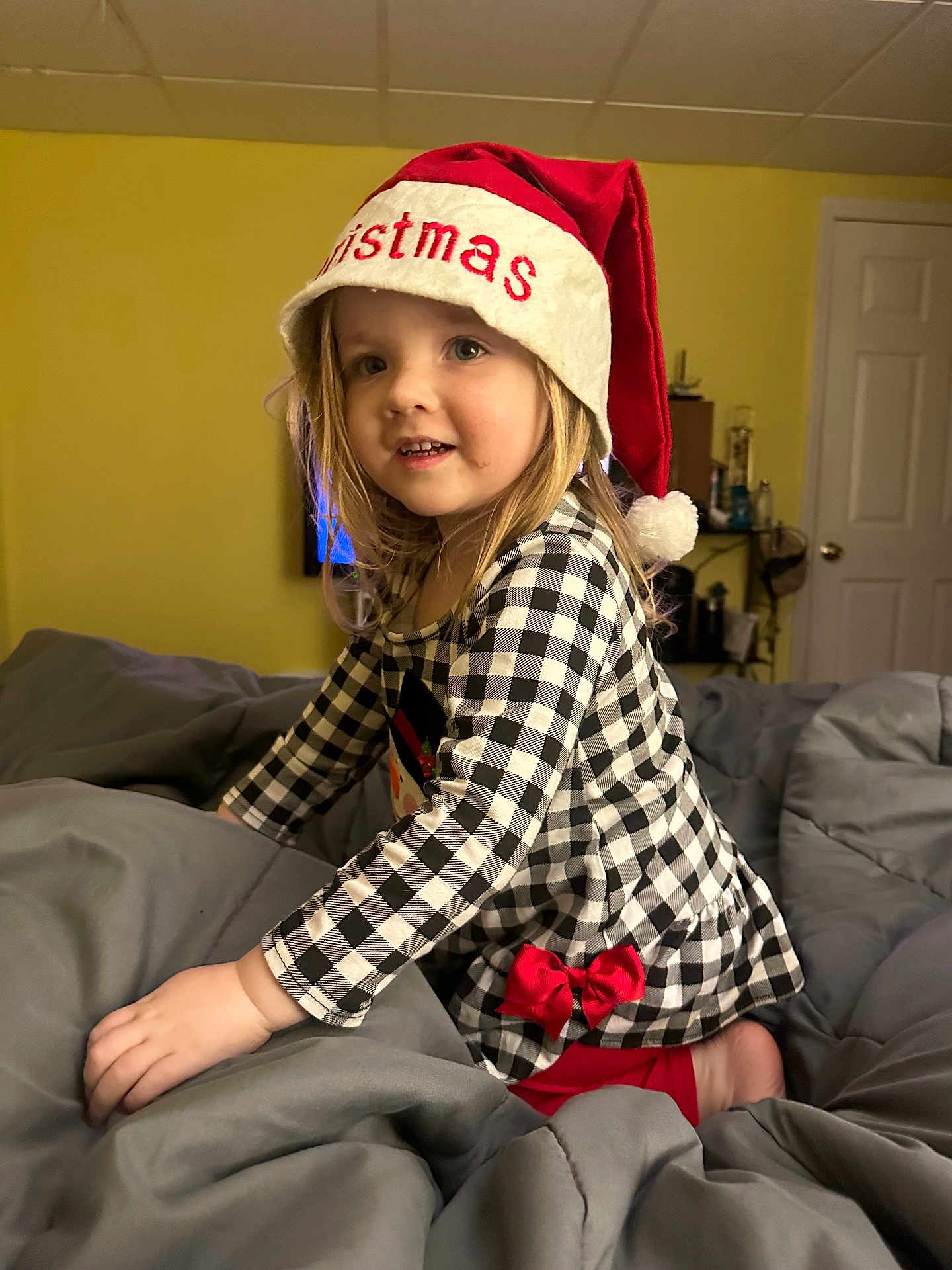 Aurora joined the competition — help win amazing prizes! child, christmas_hat, checkered_dress, red_bow, blanket, indoor, smiling, blonde_hair, bedroom, yellow_wall, door, furniture, home, holiday, festive, happy, person, portrait, cute, toddler