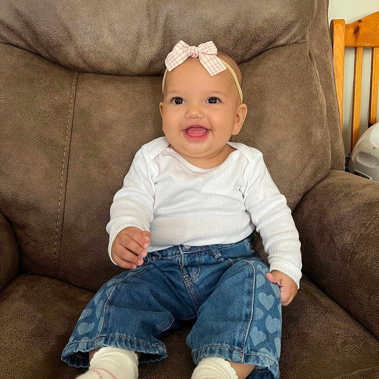 Essie is registered to the contest to win money with this photo: armchair, baby, bow, brown_furniture, child, clothing, cozy, cute, happy, headband, heart_pattern, indoor, infant, jeans, person, portrait, sitting, smiling, socks, white_shirt