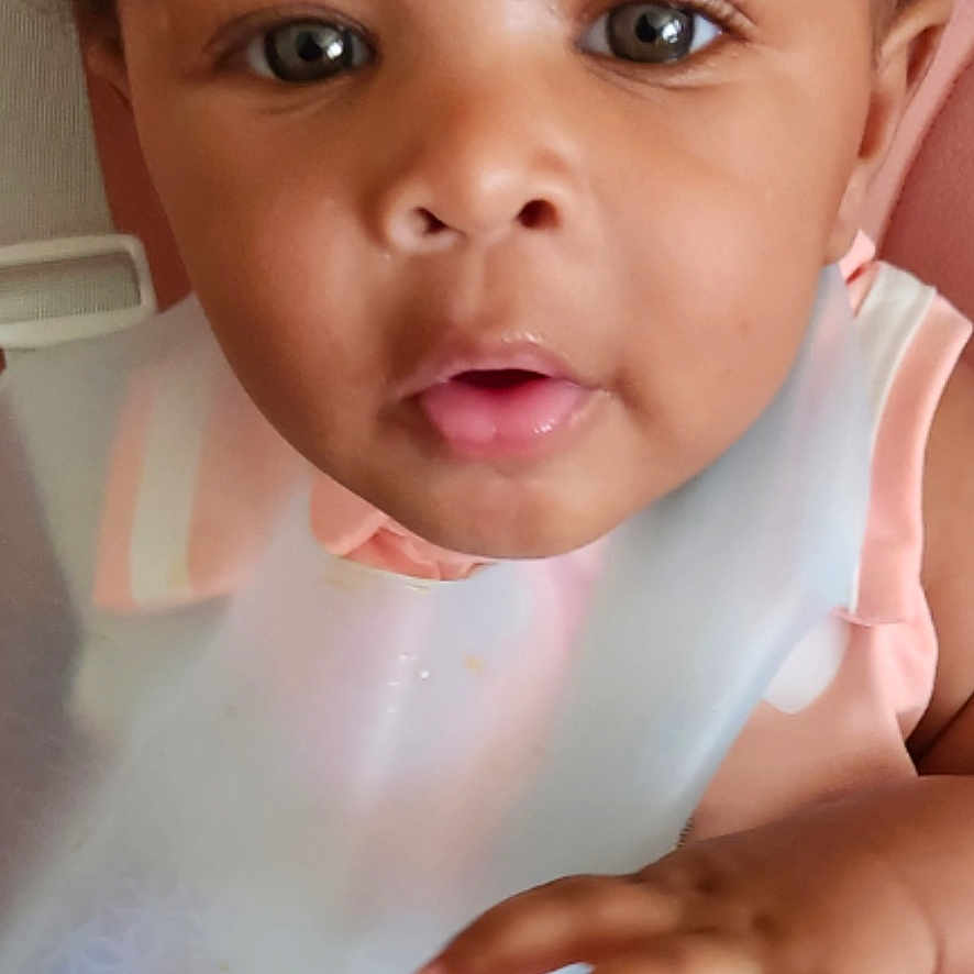 Nickole joined the competition — help win amazing prizes! baby, bib, child, closeup, clothing, curious, curly_hair, cute, expression, face, hand, indoor, infant, looking, person, pink, seat, skin, soft_light, young_child