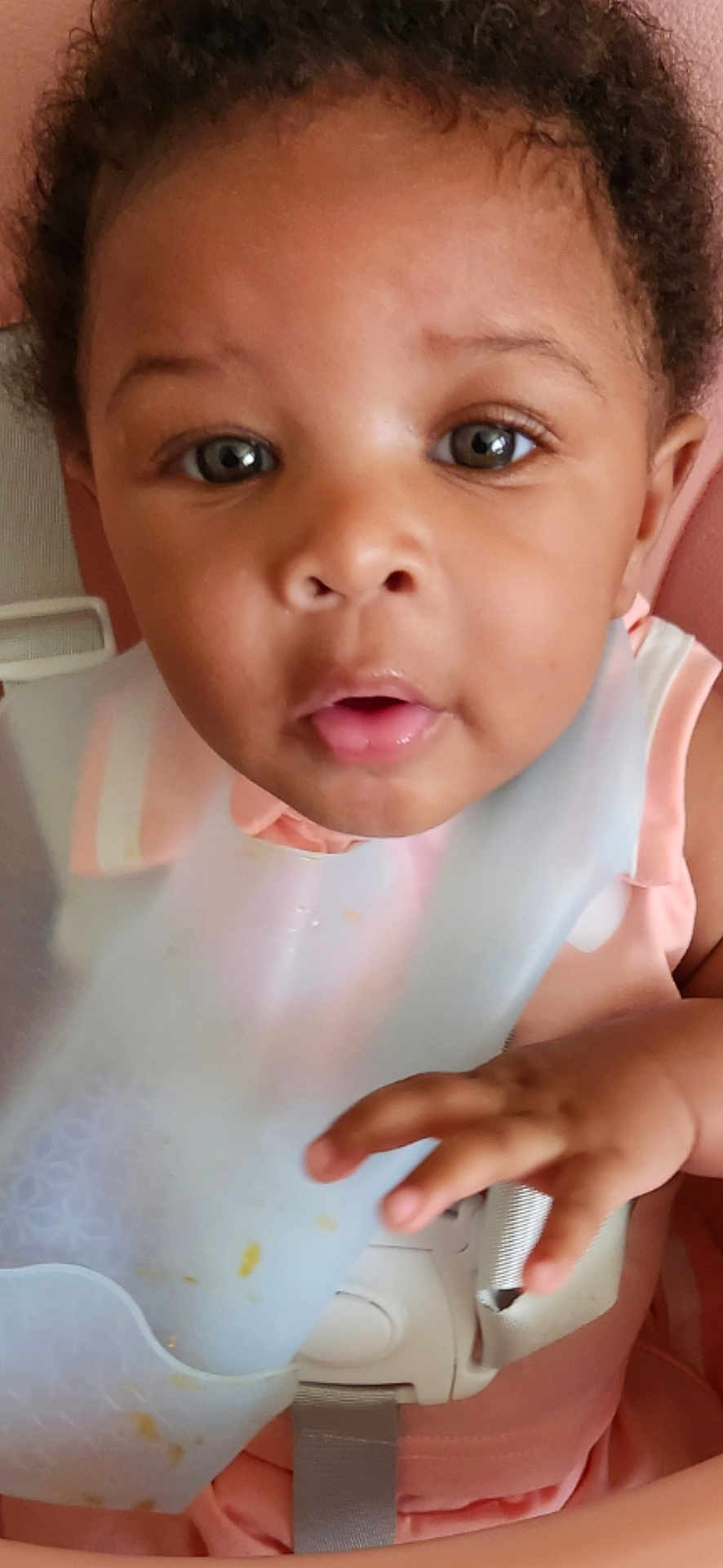 Nickole joined the competition — help win amazing prizes! baby, child, bib, face, hand, curly_hair, expression, closeup, indoor, skin, clothing, seat, infant, young_child, person, cute, looking, curious, pink, soft_light