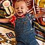 baby, denim_overalls, smiling, stuffed_animal, colorful_clothing, blanket, patterned_blanket, happy, infant, cute, lying_down, child, toy, soft_toy, fabric, portrait, indoors, small_child, playful, joyful